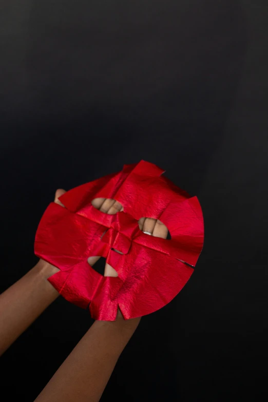 a pair of hands holding a red piece of paper, an album cover, by Ingrida Kadaka, pexels contest winner, afrofuturism, super hero mask, hands pressed together in bow, dramatic product shot, circular