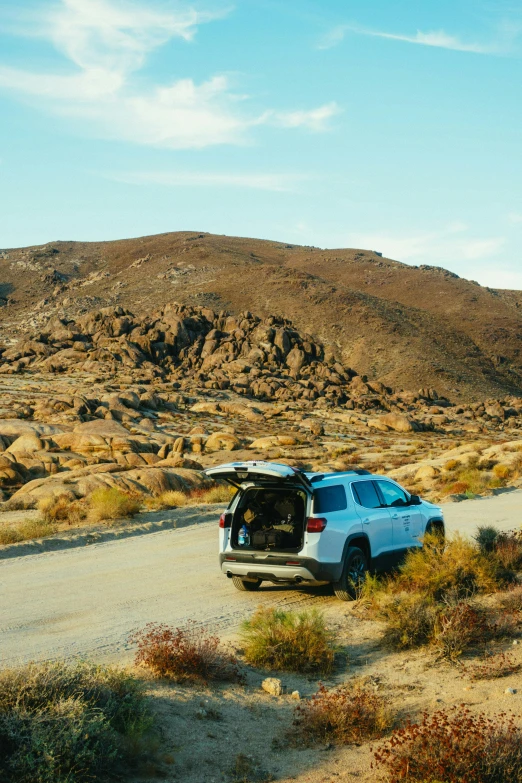 a car is parked on the side of the road, in a desert, rocky roads, boulders, campsites