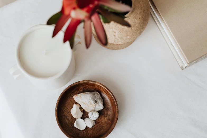 a wooden bowl sitting on top of a table next to a glass of milk, a still life, unsplash, minimalism, white stones, candle wax, botanicals, shells