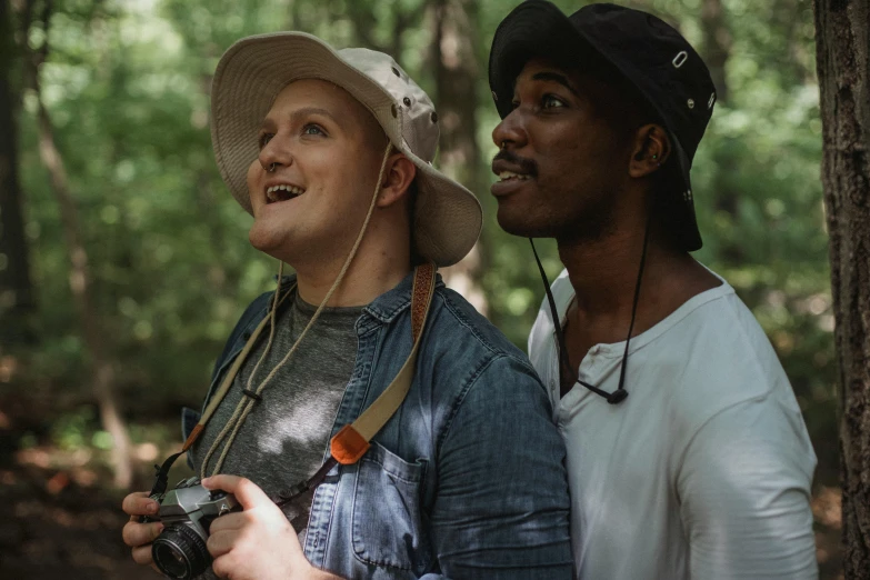 a man standing next to a woman holding a camera, in the woods, non-binary, men look up at the sky, diverse