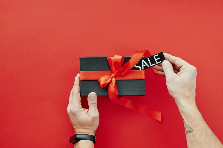 a person holding a black gift box with a red ribbon, by Julia Pishtar, pexels contest winner, magazine sales, holding a red banner, thumbnail, rectangle