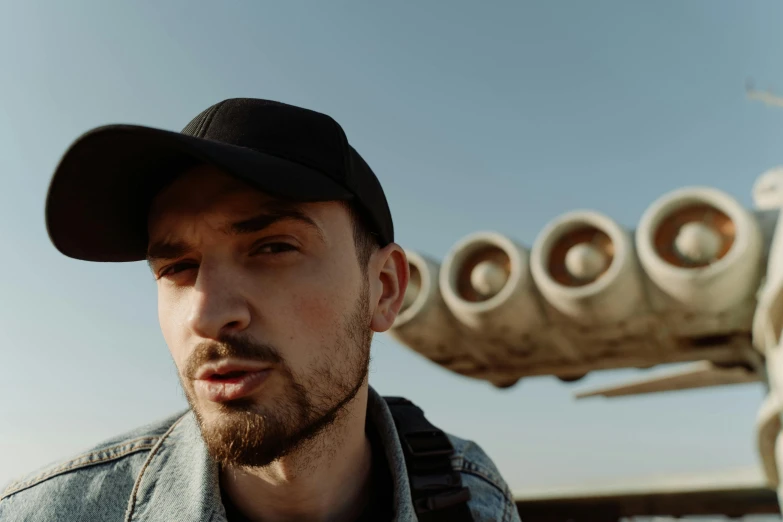 a man wearing a hat standing in front of an airplane, an album cover, pexels contest winner, photorealism, jacksepticeye, alessio albi, shot with sony alpha 1 camera, big guns