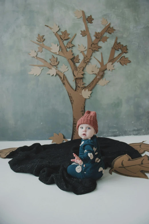 a doll sitting on the ground next to a tree, a cartoon, inspired by Elsa Beskow, trending on pexels, black beanie, studio shoot, made of cardboard, model trees