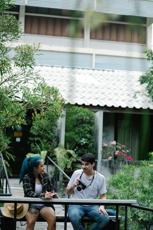 a couple of people that are sitting on a bench, in a garden of a house, holding a camera, nivanh chanthara, courtyard walkway