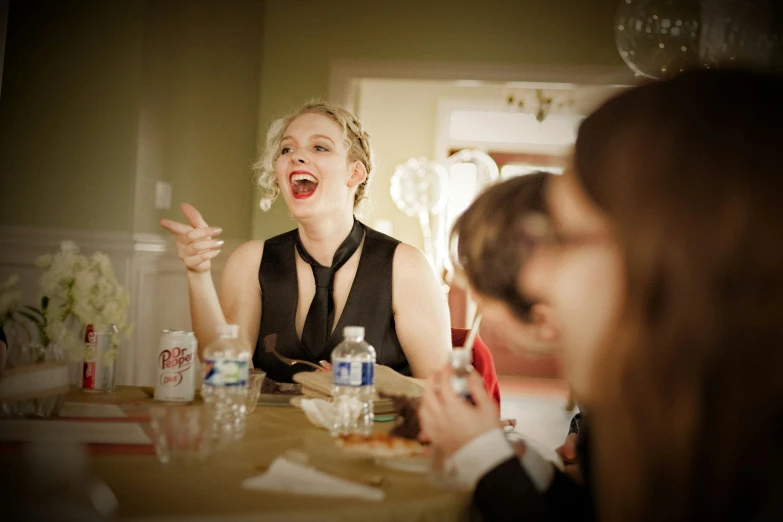 a woman in a black dress sitting at a table, by Matt Cavotta, pexels contest winner, happening, laughing hysterically, evan rachel wood, scene from a dinner party, in 2 0 1 2