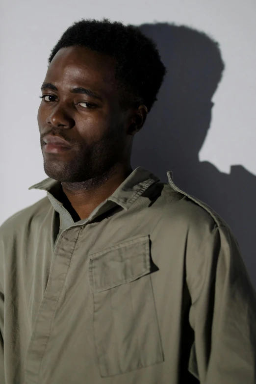 a man standing in front of a white wall, an album cover, inspired by Barthélemy Menn, hurufiyya, looking to the side off camera, very dark brown skin!, a photo of a disheveled man, backlit portrait