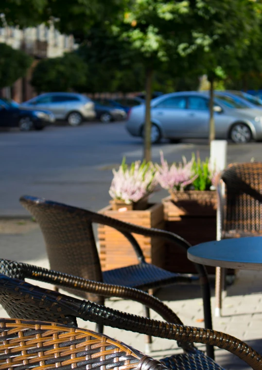a couple of chairs sitting next to each other on a sidewalk, table in front with a cup, sunny day time, square, customers