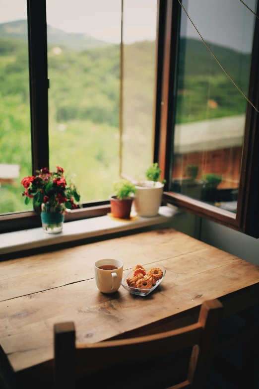 a cup of coffee sitting on top of a wooden table, a still life, by Elsa Bleda, unsplash, romanticism, bay window, overlooking a valley, small kitchen, 15081959 21121991 01012000 4k