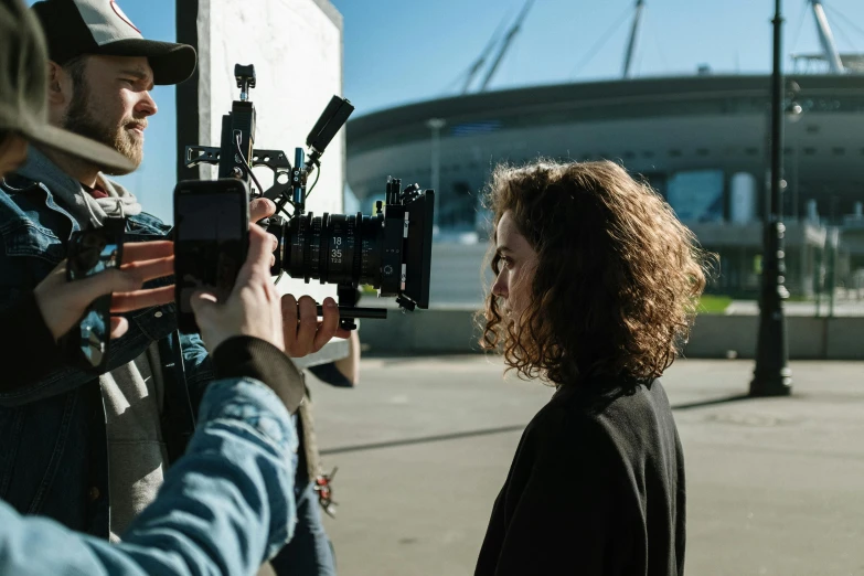 a man standing next to a woman holding a camera, nathalie emmanuel, worksafe. cinematic, sports broadcast, b - roll