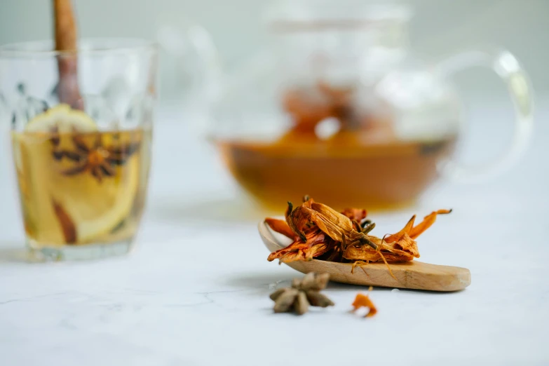 a wooden spoon sitting on top of a table next to a cup of tea, a still life, by Emma Andijewska, trending on pexels, hurufiyya, falling flower petals, holding a bottle of arak, scorpion tail, orange details