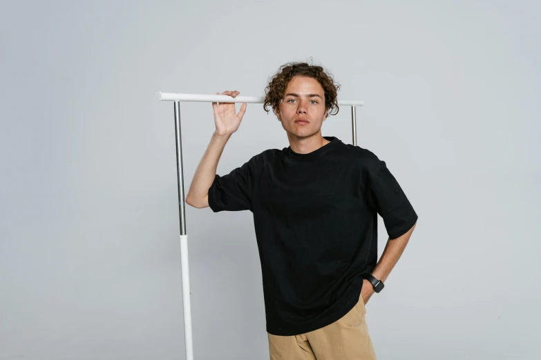 a man standing in front of a white pole, wearing black tshirt, black oversized clothes, casey cooke, eyvind