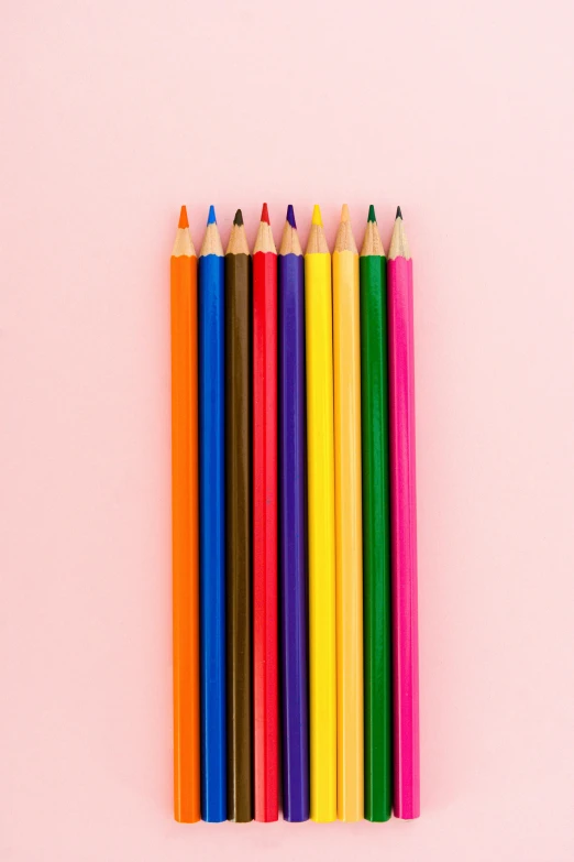 a group of colored pencils on a pink background, by Nicolette Macnamara, color photograph, medium: black pencil, multicolor, in color