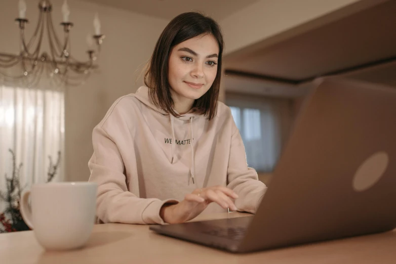 a woman sitting in front of a laptop computer, trending on pexels, beige hoodie, girl with brown hair, proportional image, uploaded