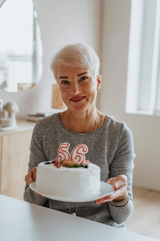 a woman sitting at a table holding a cake, pexels contest winner, he is about 6 0 years old, 2 5 6 x 2 5 6 pixels, white haired lady, he is 3 5 years old