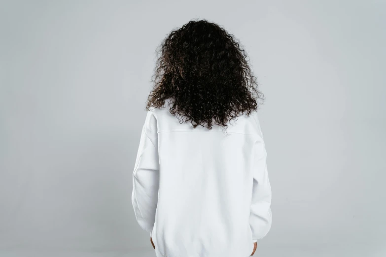 a woman with curly hair wearing a white shirt, unsplash, back view, wearing sweatshirt, blank background, low quality photo