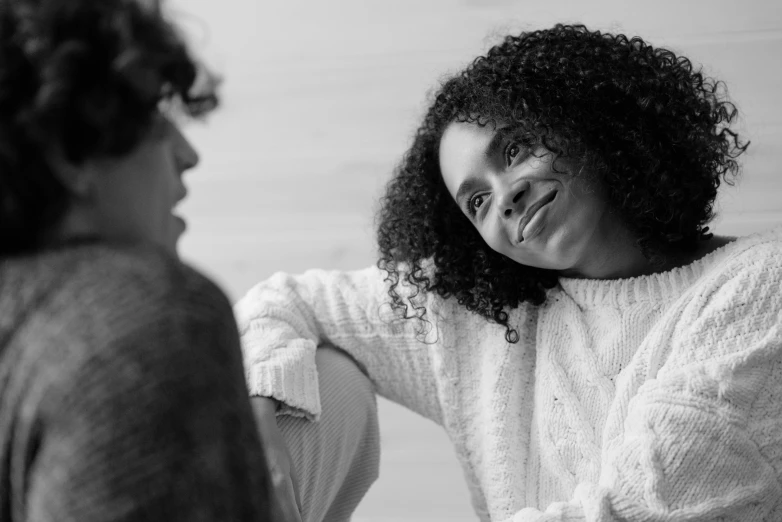 a black and white photo of a woman in a bathrobe, by Matija Jama, pexels, smiling at each other, curly afro, calmly conversing 8k, wearing a white sweater