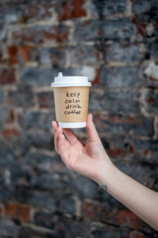 a person holding a cup of coffee in front of a brick wall, detailed product image, kek, concern, promotional image