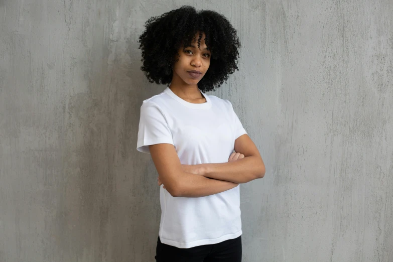 a woman standing in front of a wall with her arms crossed, by Nina Hamnett, happening, plain white tshirt, male and female, black female, no - text no - logo