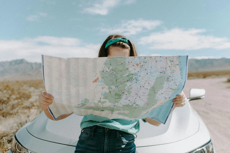 a woman standing in front of a car holding a map, by Emma Andijewska, trending on unsplash, nautical maps, panoramic view of girl, woman holding sign, navigator glasses