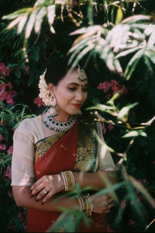 a woman in a red and gold sari, inspired by T. K. Padmini, pexels contest winner, amongst foliage, photographed on colour film, wearing elegant jewellery, cinematic outfit photo
