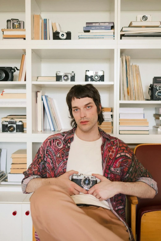 a man sitting in a chair holding a camera, queer woman, sitting on a store shelf, lucas graziano, catalog photo