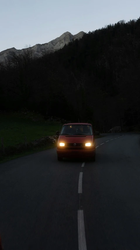 a car driving down a road with mountains in the background, by Dave Allsop, headlights are on, van, low quality photo, wales