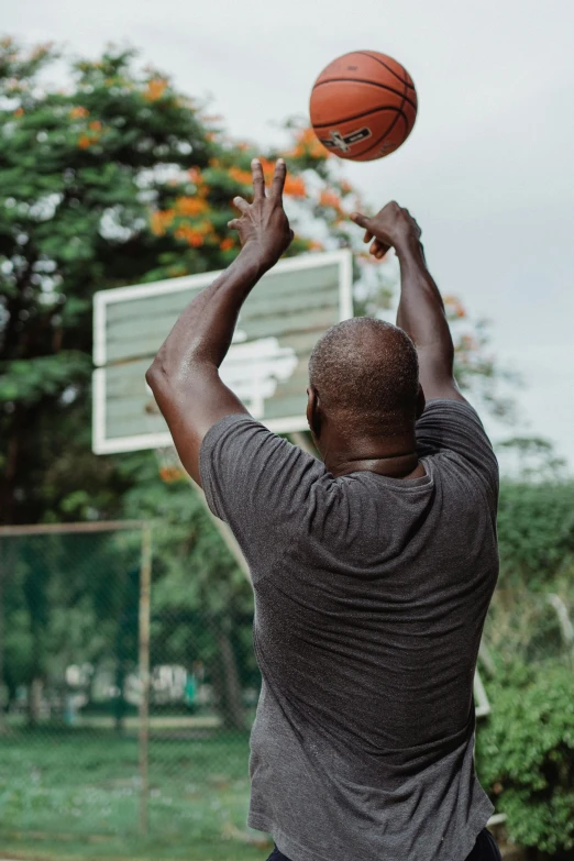 a man standing on top of a basketball court holding a basketball, happening, shot from the back, emmanuel shiru, lush surroundings, raising an arm