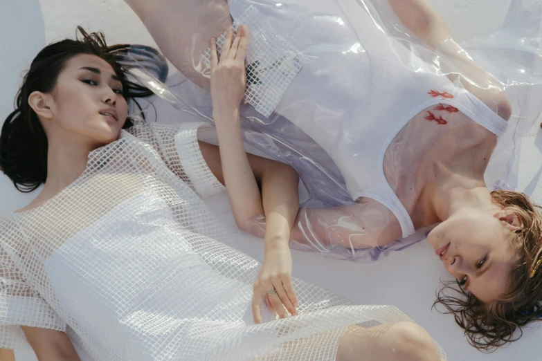 a couple of women laying on top of a bed, gutai group, wearing futuristic clothing, mesh fabrics, wearing a wet white short dress, zoomed in