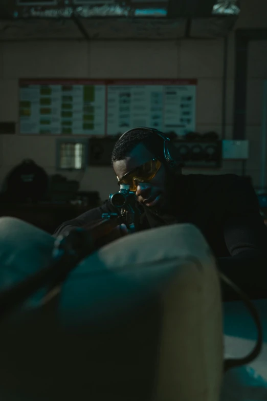 a man sitting on a couch in a dimly lit room, inspired by roger deakins, laser sights on weapons, idris elba as james bond, worksafe. cinematic, sniper
