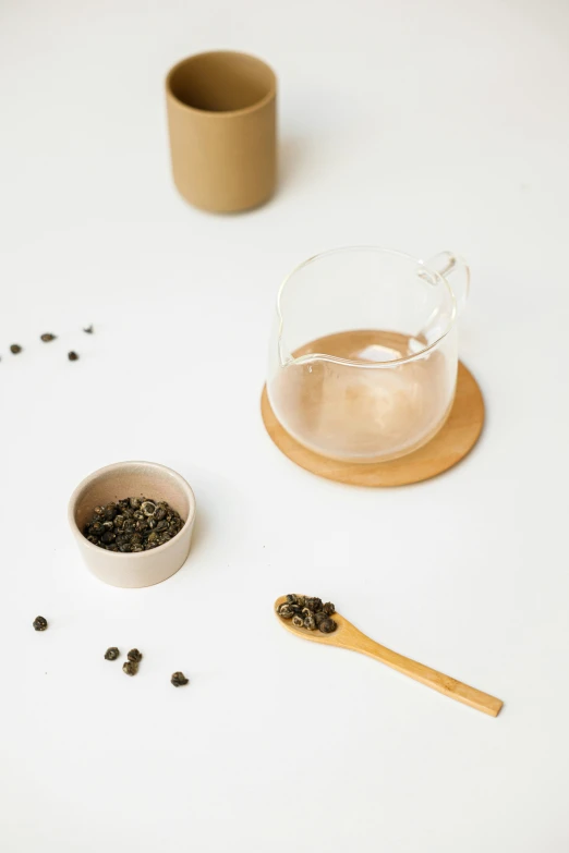 a white table topped with a cup of coffee and a wooden spoon, inspired by Cui Bai, minimalism, holding a boba milky oolong tea, glass jar, detailed product image, beige mist