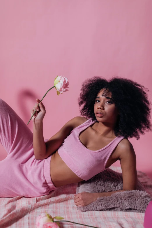 a woman laying on a bed holding a flower, by Cosmo Alexander, trending on pexels, pink clothes, with afro, cottagecore!! fitness body, concept photoset