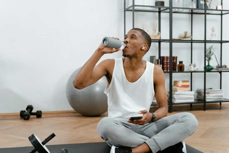 a man sitting on a yoga mat drinking from a water bottle, pexels contest winner, happening, man is with black skin, drinking a cup of coffee, people inside eating meals, lifting weights