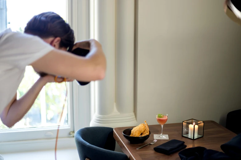 a man sitting at a table with a bowl of food in front of him, a photo, unsplash, photorealism, drinking cocktail, behind the scenes photo, photographed from behind, pr shoot