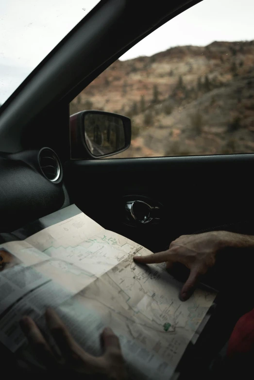 a person sitting in a car reading a map, by Daniel Seghers, pexels contest winner, moab, looking for clues, interior shot, graphic”