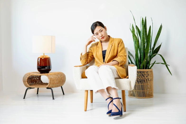 a woman sitting in a chair talking on a cell phone, inspired by Ruth Jên, pexels, minimalism, wearing open toe heels, gold and indigo, japanese collection product, wearing a blazer