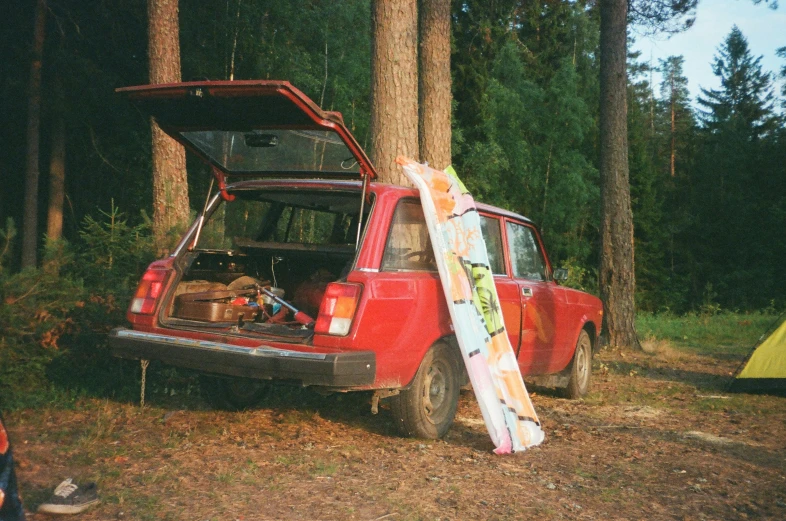 a red car with a surfboard sticking out of the trunk, by Pamela Ascherson, pine forests, 1980s photograph, daniil kudriavtsev, skateboard