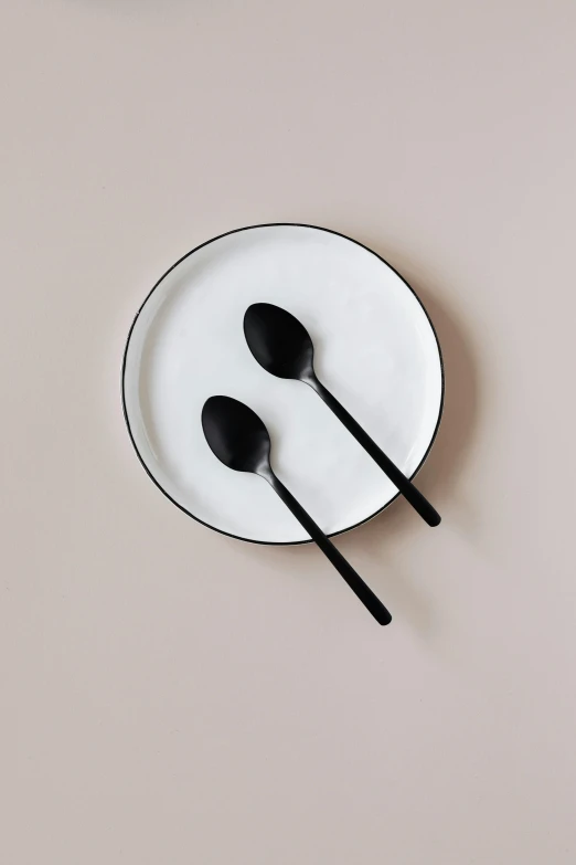 a white plate topped with two black spoons, inspired by Peter de Sève, unsplash, black matte finish, iron, 8, 3 - piece