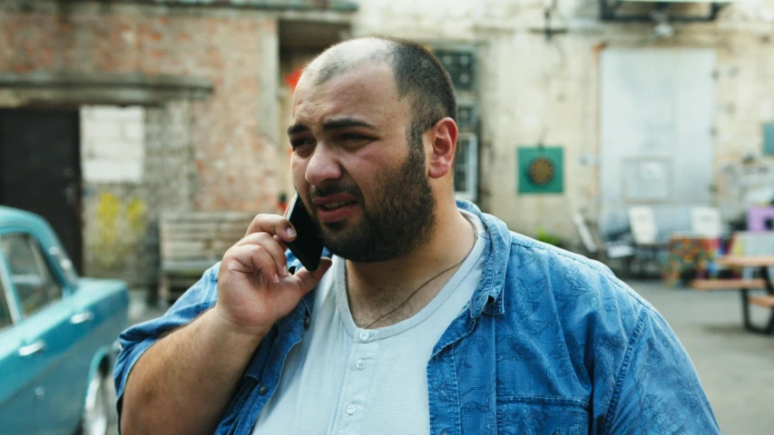 a man with a beard talking on a cell phone, by Cafer Bater, hurufiyya, still from a live action movie, an overweight, yan morala, lgbtq