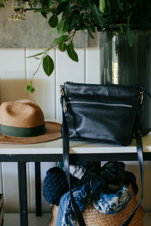 a black purse sitting on top of a table next to a hat, by Jessie Algie, dwell, lush and green, leather, hills