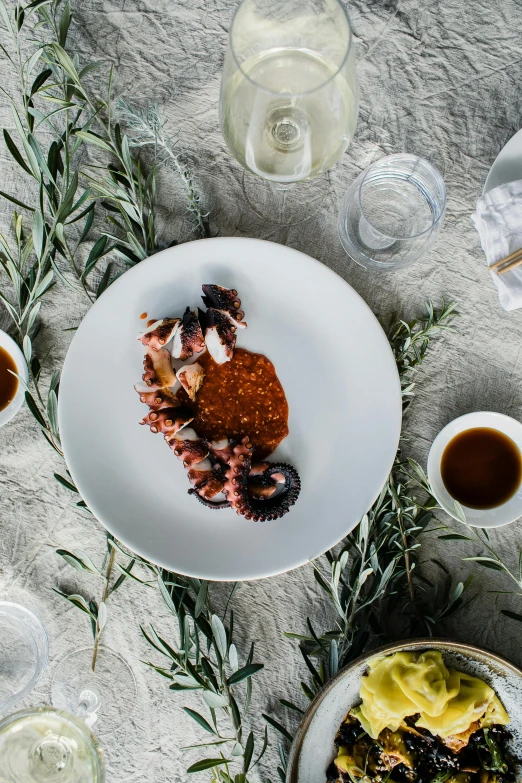 a table topped with plates of food and glasses of wine, a still life, unsplash, octopus tentacles, white, honey, ultra textured