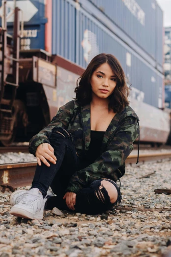 a woman sitting on the ground in front of a train, a portrait, by Robbie Trevino, trending on pexels, wearing camo, yzy gap, asian girl, confident looking