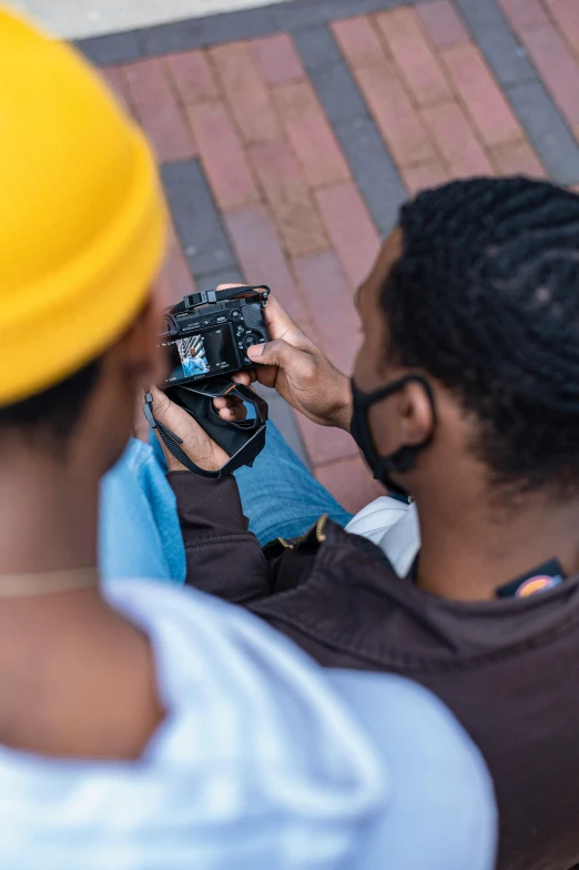 a man taking a picture of another man with a camera, looking down on the camera, shot with sony alpha 1 camera, two young men, coloured