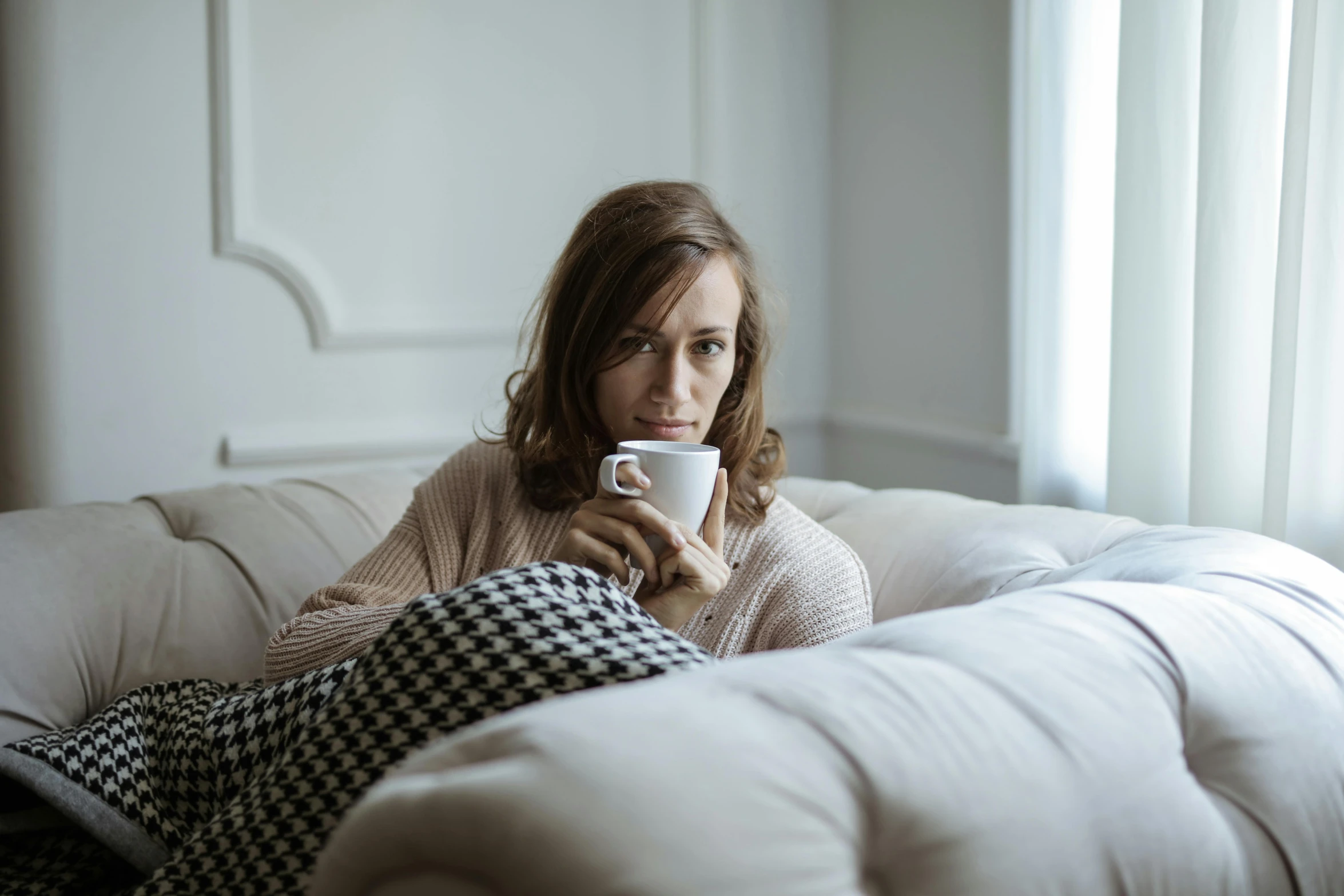 a woman sitting on a couch holding a cup, by Alice Mason, trending on pexels, happening, sick with a cold, attractive brown hair woman, anna nikonova aka newmilky, a single