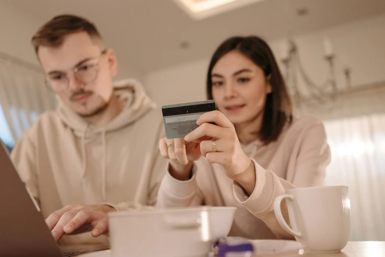 a man and a woman sitting at a table with a laptop and a credit card, by Adam Marczyński, pexels contest winner, avatar image, woman holding another woman, holding a very advance phone, animation