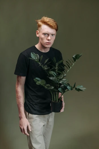 a man standing with a plant in his hand, an album cover, inspired by Lasar Segall, pexels contest winner, hyperrealism, hr ginger, wearing black tshirt, non binary model, plant predator