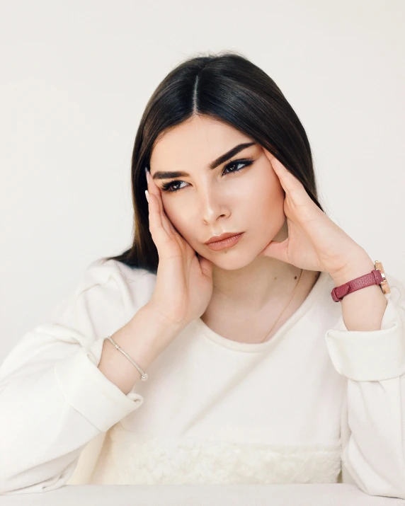 a woman sitting at a table with her hands on her face, trending on pexels, nonbinary model, on a pale background, ukrainian girl, soft but grumpy