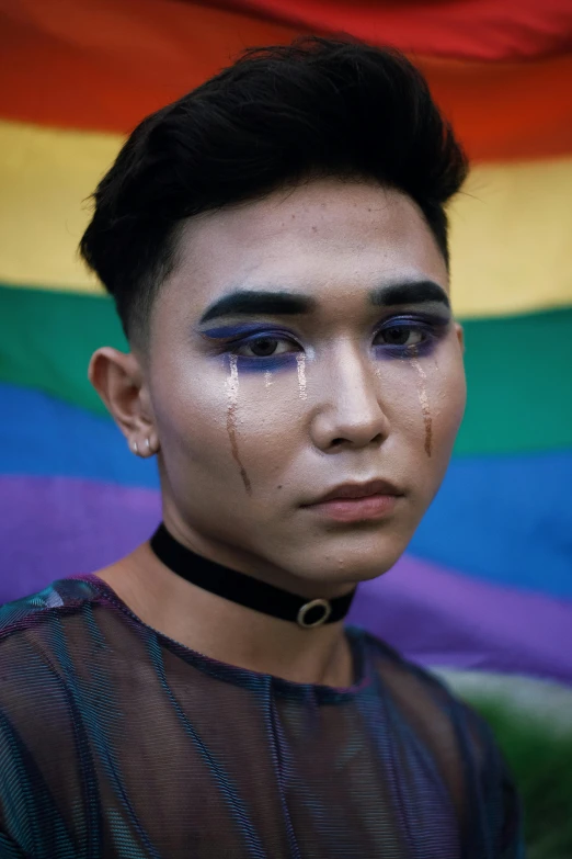 a man standing in front of a rainbow flag, by Robbie Trevino, crying makeup, hong june hyung, 18 years old, on black background