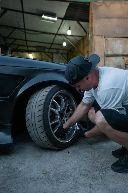 a man working on a car tire in a garage, a portrait, featured on reddit, high body detail, half turned around, performance, profile image
