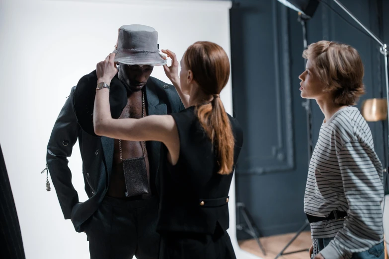 a woman standing next to a man in a suit and tie, by Adam Marczyński, pexels contest winner, photorealism, wearing a hat, behind the scenes photo, photoshoot for skincare brand, wearing a vest top