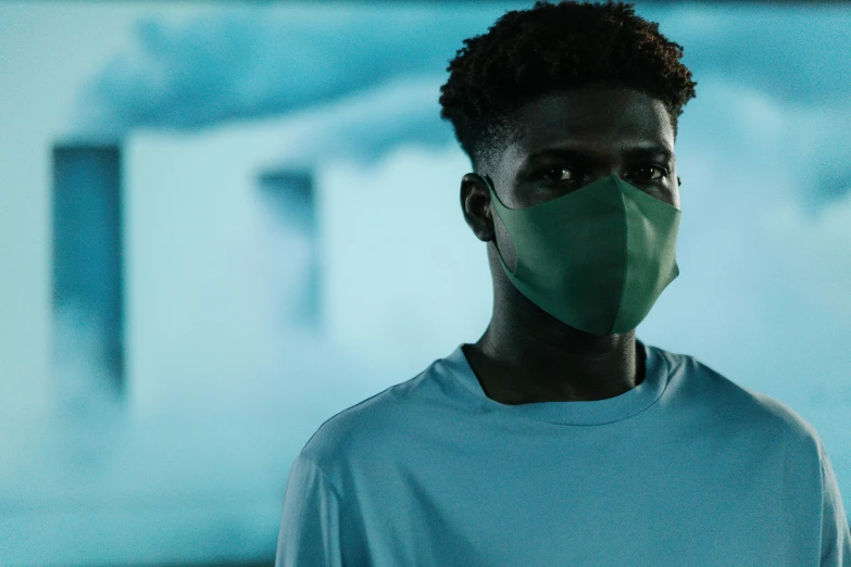 a close up of a person wearing a face mask, pexels contest winner, afrofuturism, sea - green and white clothes, standing in a dimly lit room, meet the actor behind the scenes, outlive streetwear collection